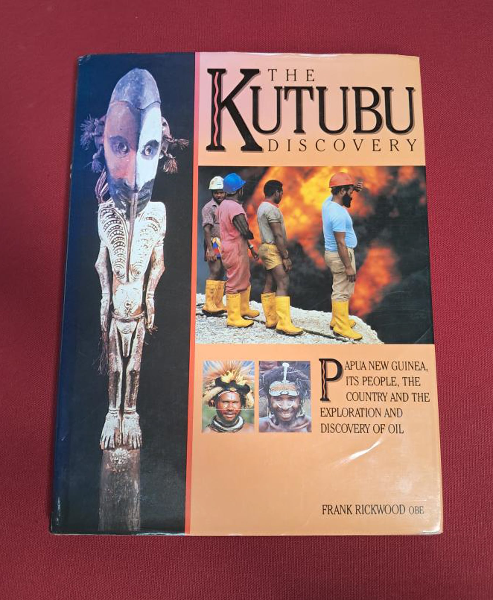 Kutubu Discovery. An orange cover, with a photo of 4 men staring at a fire in the centre. On the left hand side is a tribal mask or statue.